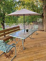 Patio umbrella fully opened over a glass outdoor table with metal chairs and a wooden bench on a wooden deck.