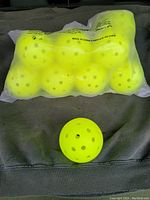 Clear image showing a sealed bag containing ten bright yellow perforated plastic balls, with one ball outside the bag placed on a surface.