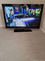 Front view of Samsung LCD TV turned on, showing a news broadcast with female anchors.