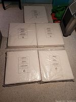 Photo showing five seat cushions sealed in original plastic wrap, arranged on carpeted floor.