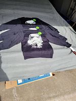 Three Star Wars boys' sweatshirts laid flat on a surface, showing front graphics and glow-in-the-dark feature stickers.