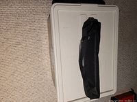 Closed tripod inside black carrying case resting on white plastic chest