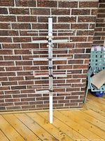 Samsung digital TV antenna standing vertically against a brick wall on a wooden deck, showing full front view with silver horizontal rods and white mounting tube.