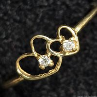 Close-up front view of 10kt gold ring with two small diamonds in open heart design on a black background.