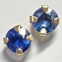 Close-up of two round faceted blue sapphire gemstones in 10kt yellow gold four-prong settings.
