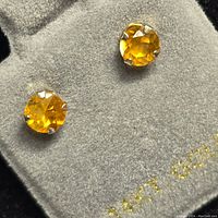 Close-up photo of the two round faceted citrine earrings set in 14kt gold on a grey velvet background showing the color and cut of the stones and the gold stamp.
