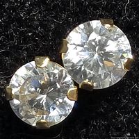 Close-up photo showing round cubic zirconia stone in 14kt gold four-prong setting against black background.