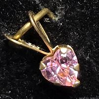 Close-up of heart-shaped pink cubic zirconia stone in 14kt gold setting showing detail of prongs and bail.