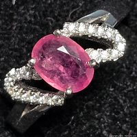 Close-up front view of the sterling silver ring showcasing the oval pink/red ruby and the sparkly clear stones on each side.