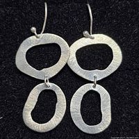 Front view of two sterling silver earrings showing connected irregular open oval shapes and textured finish.