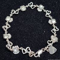 Top view of the entire sterling silver bracelet laid out flat on a black background showing heart and floral motifs with clasp and heart tag.