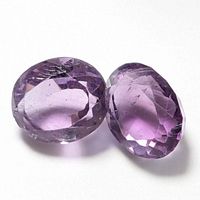 Pair of oval faceted purple amethyst gemstones photographed on a white background showing clarity and color.