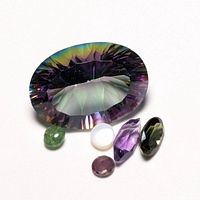 Six assorted genuine gemstones displayed on white background with various cuts and colors including a large oval multicolor gem.