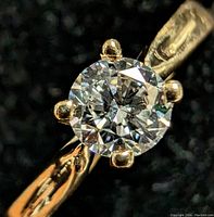 Close-up of round brilliant diamond and six-prong setting against black background