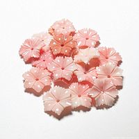 Close-up photo showing the detailed carving of several small coral flowers in varying shades of pink and red with a hole in the center for jewelry making.