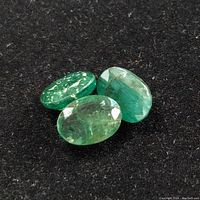 Three oval loose emerald gemstones with faceting and minor inclusions on a black background.