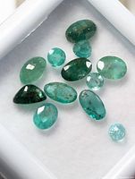 Top view of loose emerald gemstones in a display box showing various cuts and green shades.