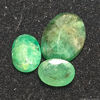 Three emerald gemstones arranged on a black background showing different sizes and green hues.