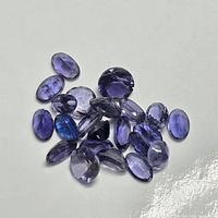Multiple faceted iolite stones laid out on a white background, displaying their varying shapes and violet-blue colors.