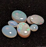 Six loose oval polished opal gemstones on black background showing play-of-color effects.