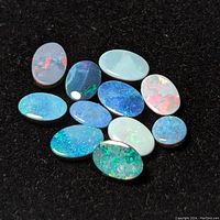 Image showing 12 oval polished opal stones on black background with vibrant color play.