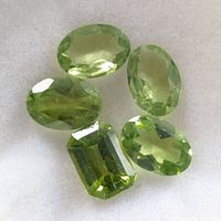 Five light green faceted peridot gemstones displayed together to show shape and color.