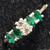 Close-up view of sterling silver ring showing green and clear stones from an angle.