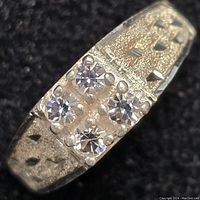 Close-up front view of sterling silver ring showing four clear round stones in square setting and textured band with triangular cut-outs.