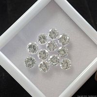 Top-down photo showing 11 loose white cubic zirconia stones arranged on a white surface inside a tray.