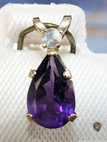 Front view of the pendant showing the pear-shaped deep purple amethyst and small round white gemstone in 10K gold setting.