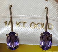 Close-up front view of the earrings showing the amethyst stones and 10K gold marking in the background.