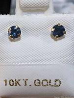 Close-up of the sapphire stud earrings set in 10K gold fill backing, showing deep blue color and prong setting.