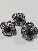 Three pieces (ring top and two earrings) front view showing sapphire cabochons and black accent stones