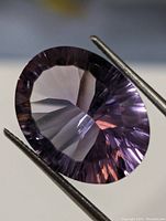Close-up image of a round faceted amethyst held by tweezers showing the gemstone's cut, color, and clarity.
