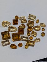 Multiple genuine citrine gemstones in various shapes and colors spread on white background.