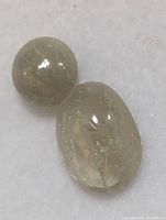Two genuine color change Zultanite cabochon cut stones placed on a white background. One round and one oval, visible natural inclusions.