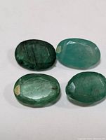 Set of four oval-shaped faceted emerald gemstones with visible inclusions and varying green shades.