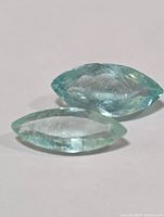 Photo of two marquise cut genuine emerald gemstones showing light green color and surface inclusions.