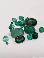 Overview of multiple loose emerald gemstones of varying sizes and shapes on a white background.