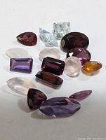 Assorted genuine faceted gemstones in various cuts and colors placed on a light background showing size and shape variety.