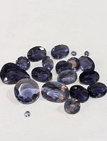 Photo showing multiple faceted genuine iolite gemstones in various shapes and sizes on a white background.