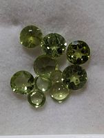 Photo showing eight genuine peridot gemstones in various faceted round and pear shapes with light olive green coloring on a white background.