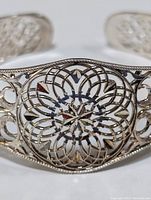 Close-up of filigree floral pattern on the front center of the silver open cuff bangle bracelet