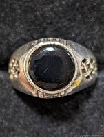 Front view showing black onyx cabochon set in silver ring with decorative sides and textured bezel.