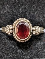 Close-up front view of silver ring with faceted oval red gemstone on black background