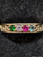 Close-up front view of the silver ring showing the four colored stones: green, light pink, deep pink, and light blue, with carved patterns on band.