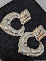 Photo of sterling silver heart-shaped earrings with leaf-like top elements placed on black background.