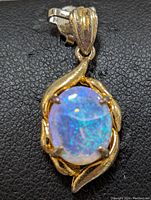 Close-up of oval blue opal gemstone set in sterling silver pendant with decorative prong setting and flowing silver accents.
