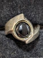 Front angle of a sterling silver ring with a glossy round black onyx stone set in a modern asymmetric silver band.