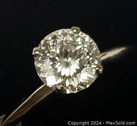 Close-up front view of the round moissanite stone in a four-prong yellow gold setting on the ring band.